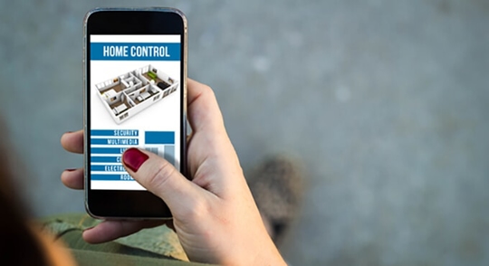 A person is holding a smartphone showing a home control app with a floor plan and menu options.