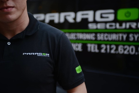 A person wearing a black polo shirt with the Paragon Security logo.